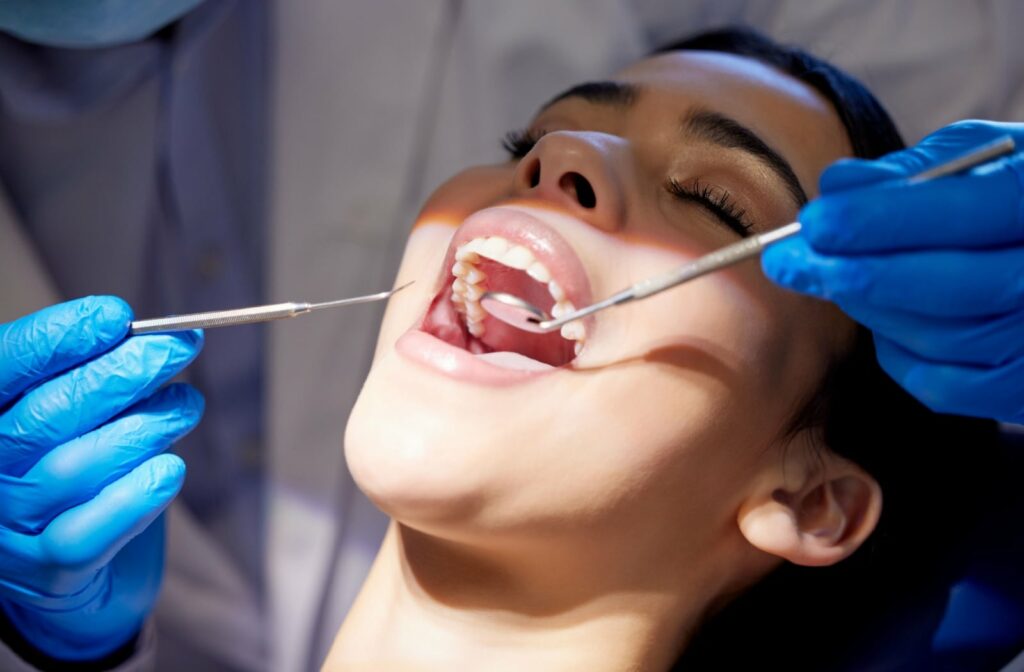 Patient undergoing a dental examination with mirror and scaler instruments during a routine check-up